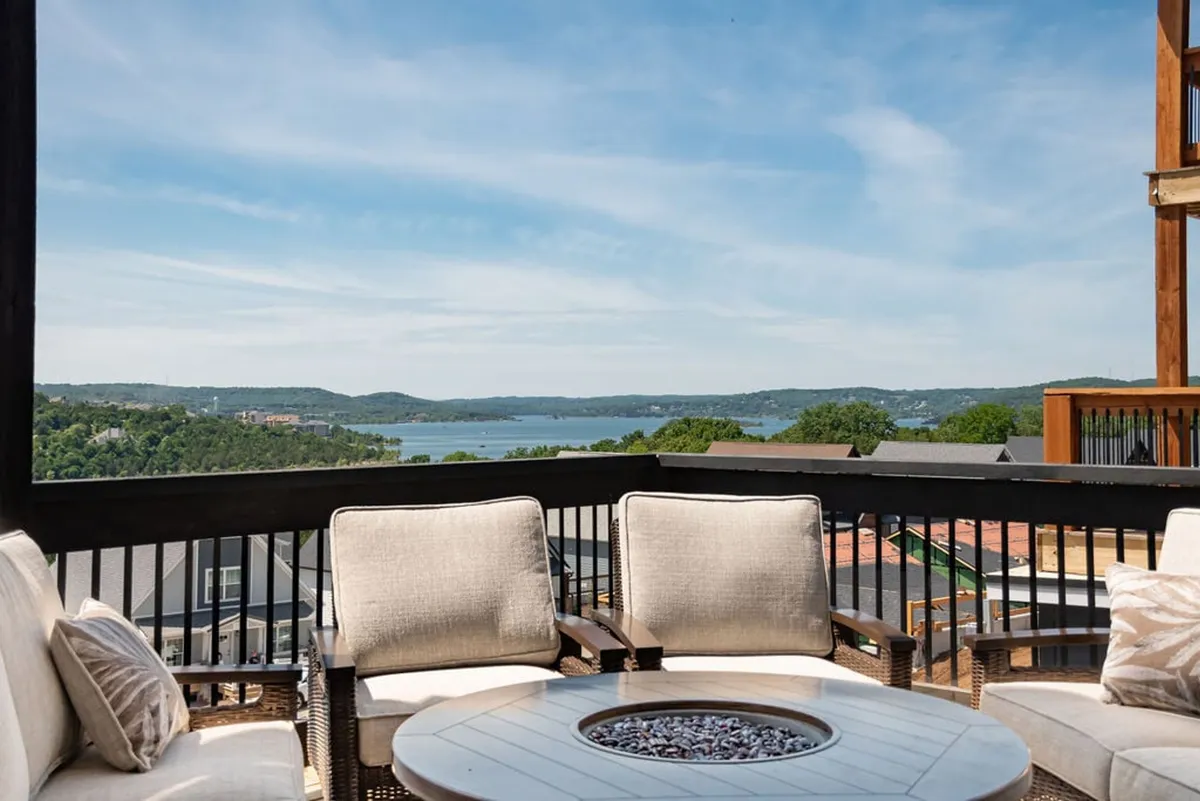 An inviting exterior space features a fire pit surrounded by cozy seating, set against a backdrop of a sparkling lake and lush greenery. The scene is perfect for socializing, enjoying a lakeside sunset, or stargazing in the evening, encapsulating a friendly, relaxed, and celebratory vibe.