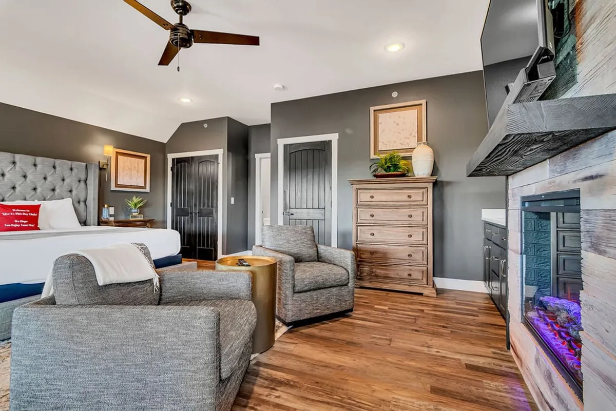 A tranquil bedroom suite with a large bed, decorative artwork, a cozy seating area with armchairs, and a fireplace—creating an inviting spot for relaxation. The design features plush bedding, warm lighting, and space to enjoy morning coffee or a quiet evening by the fire.