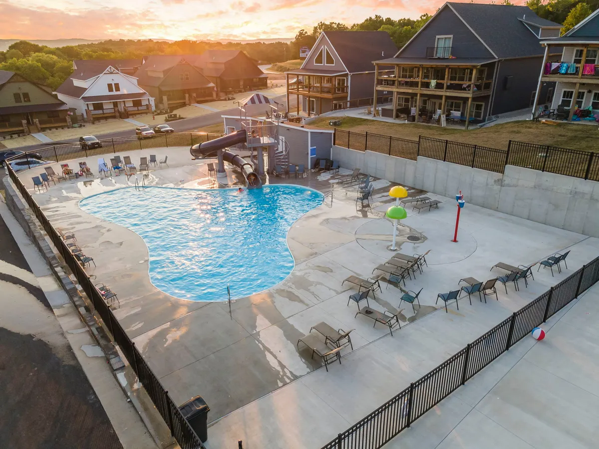 A lively exterior scene centered around the resort's main outdoor swimming pool, with a prominent water slide, inviting lounge chairs, and playful water features. Children and families are visible enjoying the water, while others relax poolside as the sun sets, encapsulating the vibrant, social side of Branson Cove's amenities.