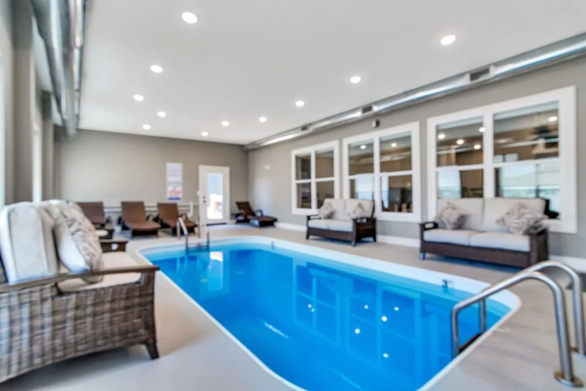 An inviting indoor swimming pool area with comfortable seating and large windows that fill the space with natural light. The tranquil setting is perfect for year-round swimming, unwinding, and social gatherings, regardless of the weather outside.