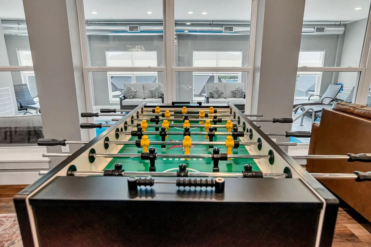 The image highlights a foosball table set near large windows and a cozy seating area, creating a bright, energetic space. The combination of natural light and leisure elements embodies friendly competition and laid-back hangouts.