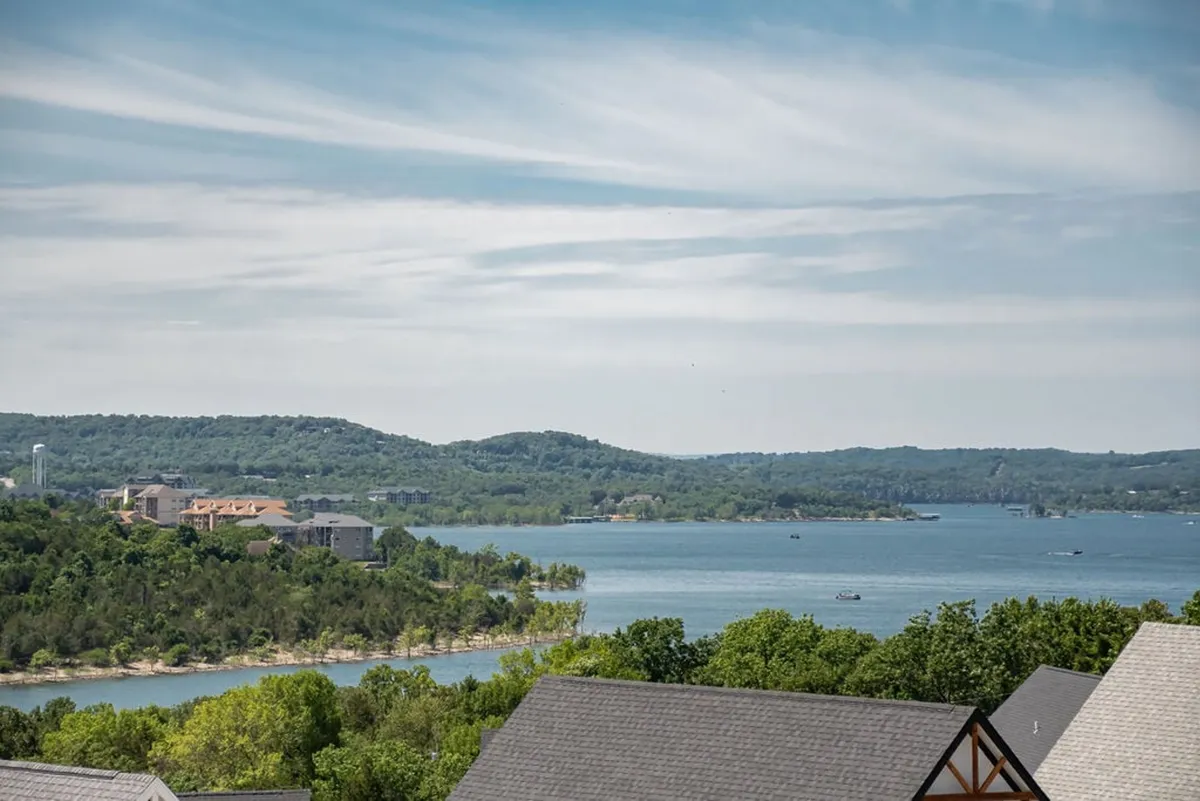 A tranquil view of Table Rock Lake with gentle hills in the background and a few boats dotting the water. Trees line the shore, and the sky is reflected in the calm surface of the lake, evoking a sense of relaxation and outdoor enjoyment.