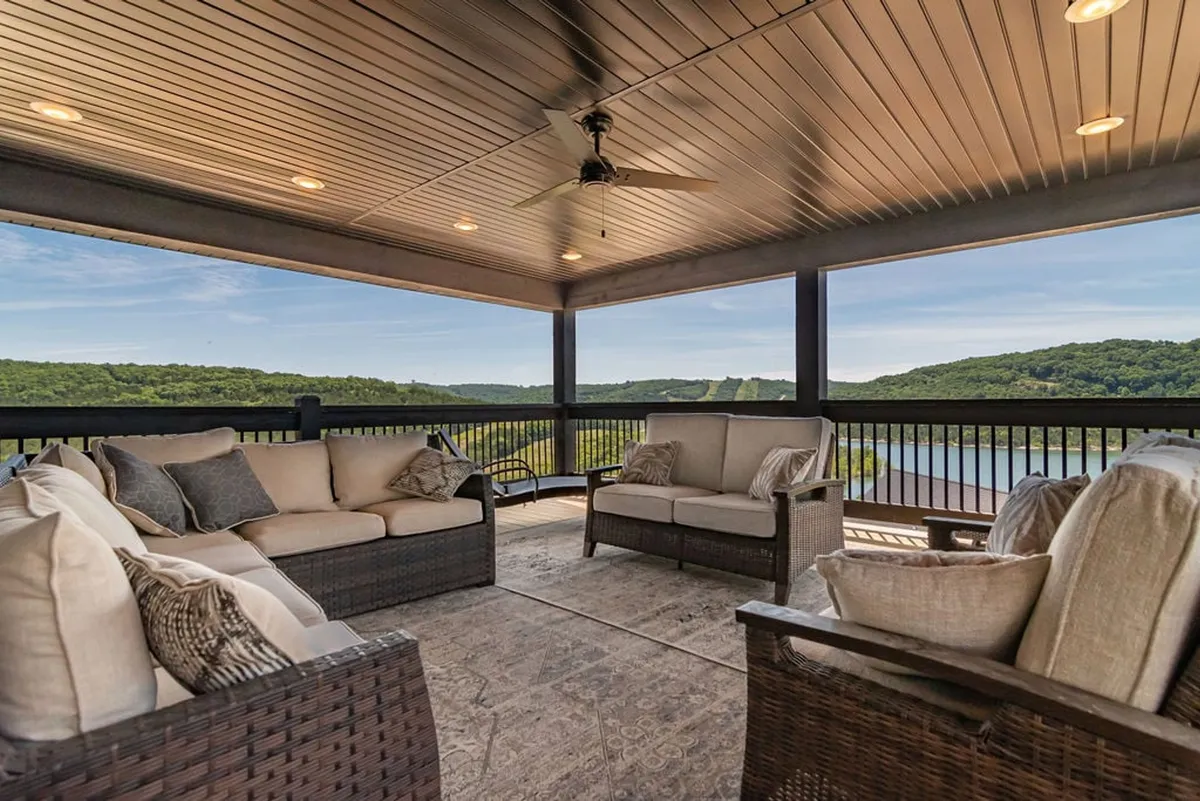 A beautifully arranged exterior lounge area features comfortable seating and a decorative rug overlooking sweeping hills and a tranquil body of water. This inviting space is designed for relaxation with panoramic views, making it ideal for enjoying a morning coffee, sunset toast, or social gatherings under the open sky.