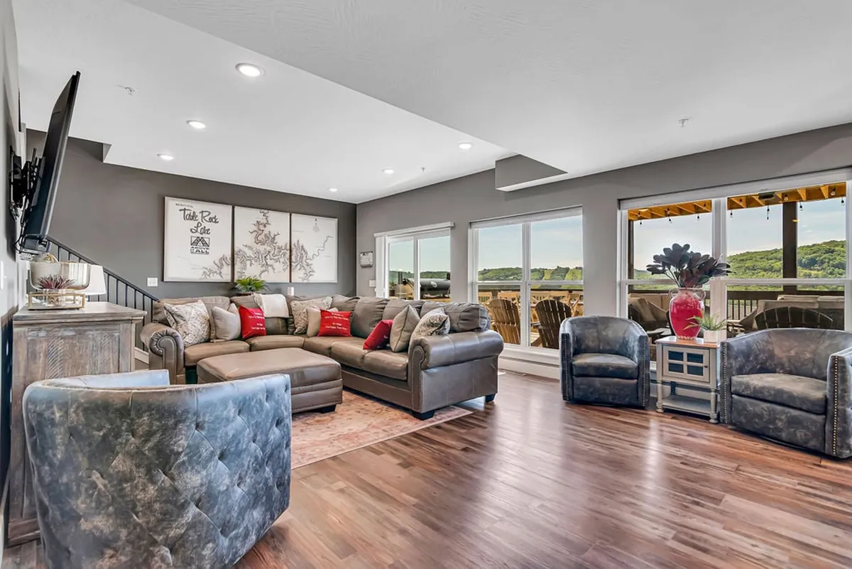 A cozy living area featuring a large sectional sofa, decorative chairs, and expansive windows offering picturesque views. The arrangement is geared toward social gatherings, family relaxation, and sunset watching, echoing the atmosphere of comfort and togetherness.