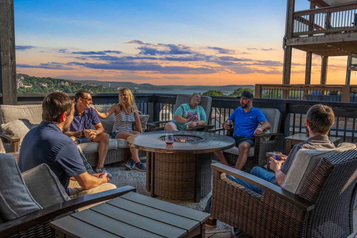 The image showcases a cozy fire pit surrounded by comfortable seating, with a group of people laughing and sharing drinks as the sun sets over a breathtaking lake view. The scene exudes warmth, camaraderie, and the promise of unforgettable evenings in a beautiful, private setting.